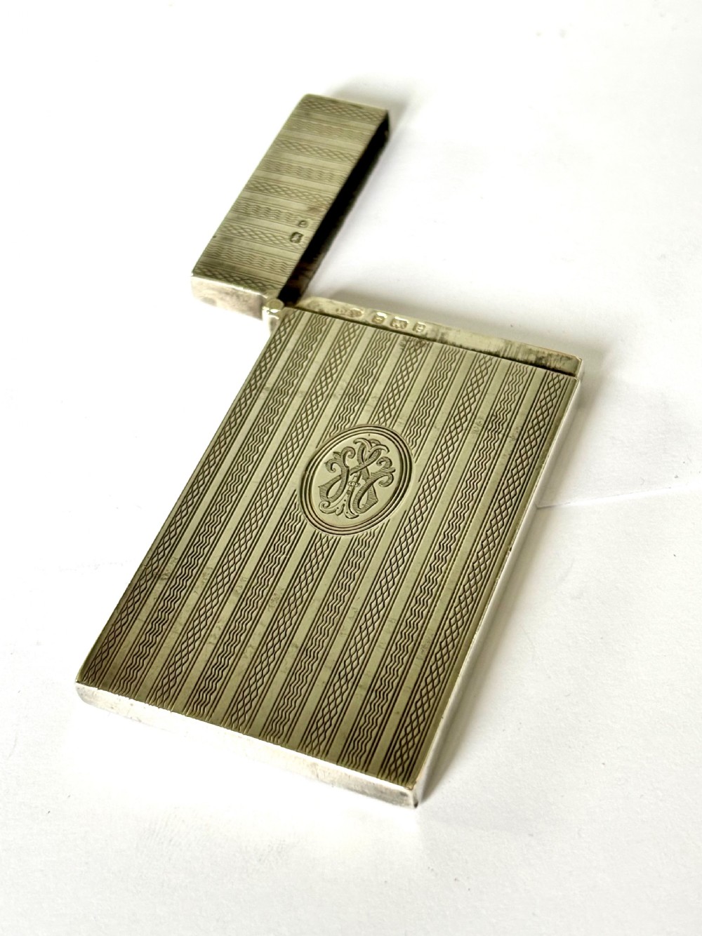 An Edwardian sterling silver slimline calling card case featuring vertical engine-turned stripes and a central oval monogram cartouche. View VII