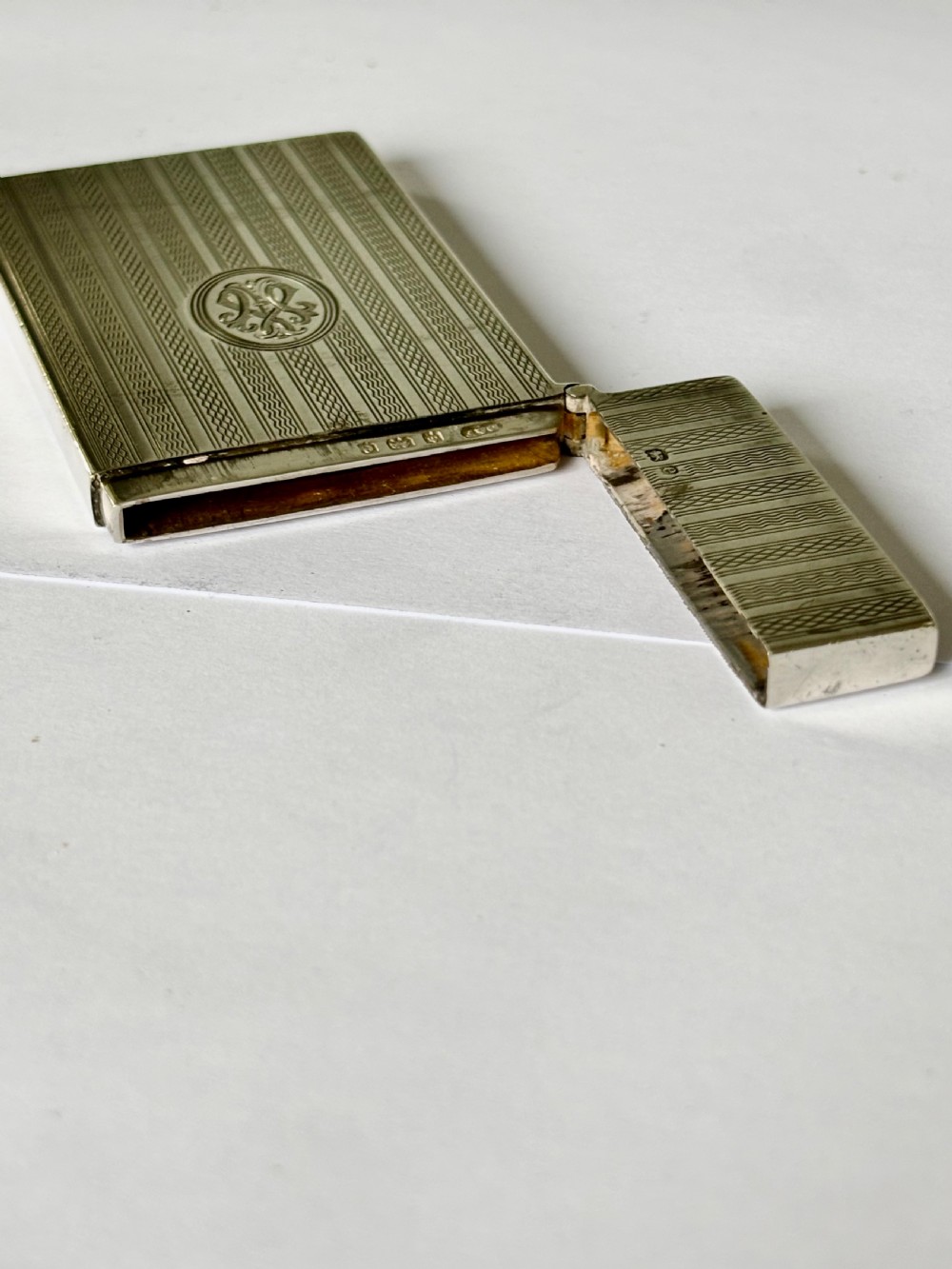An Edwardian sterling silver slimline calling card case featuring vertical engine-turned stripes and a central oval monogram cartouche. View IX