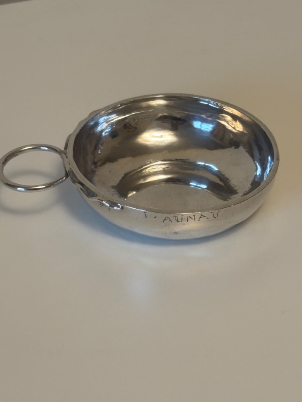 A shallow 19th-century French silver wine taster featuring a loop handle and engraved lettering on the outer rim.