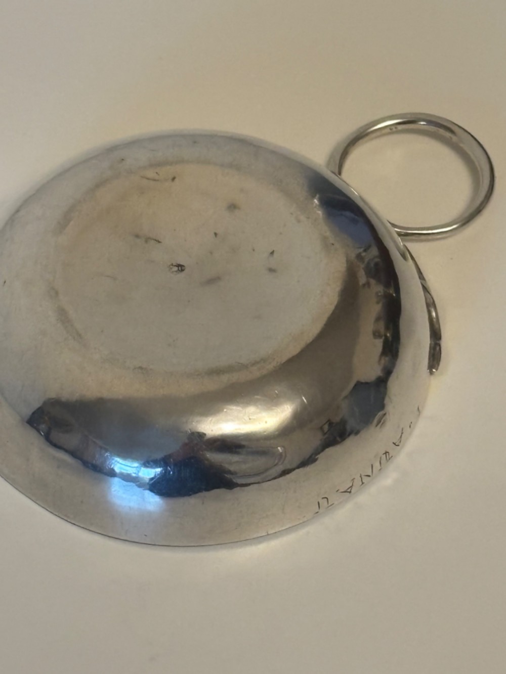 A shallow 19th-century French silver wine taster featuring a loop handle and engraved lettering on the outer rim. View VI