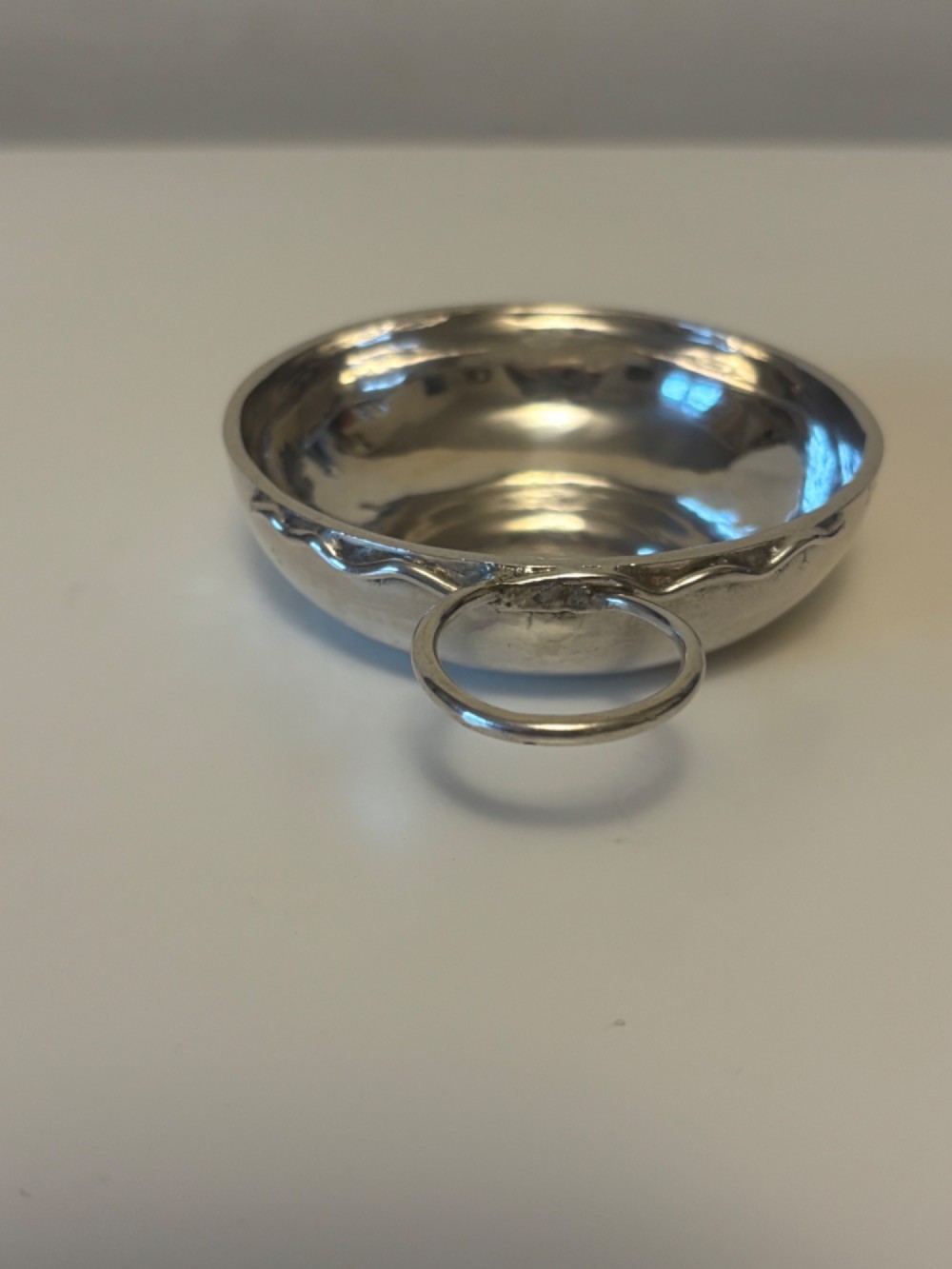 A shallow 19th-century French silver wine taster featuring a loop handle and engraved lettering on the outer rim. View X
