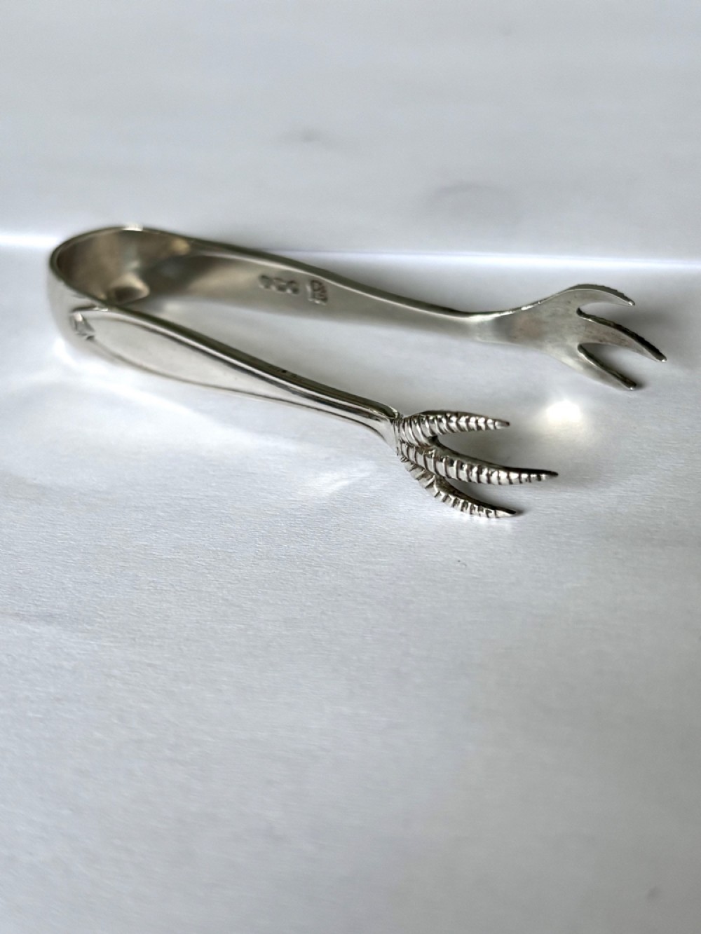 A pair of hallmarked sterling silver sugar nips featuring curved arms and claw-shaped grips resting on a light surface.