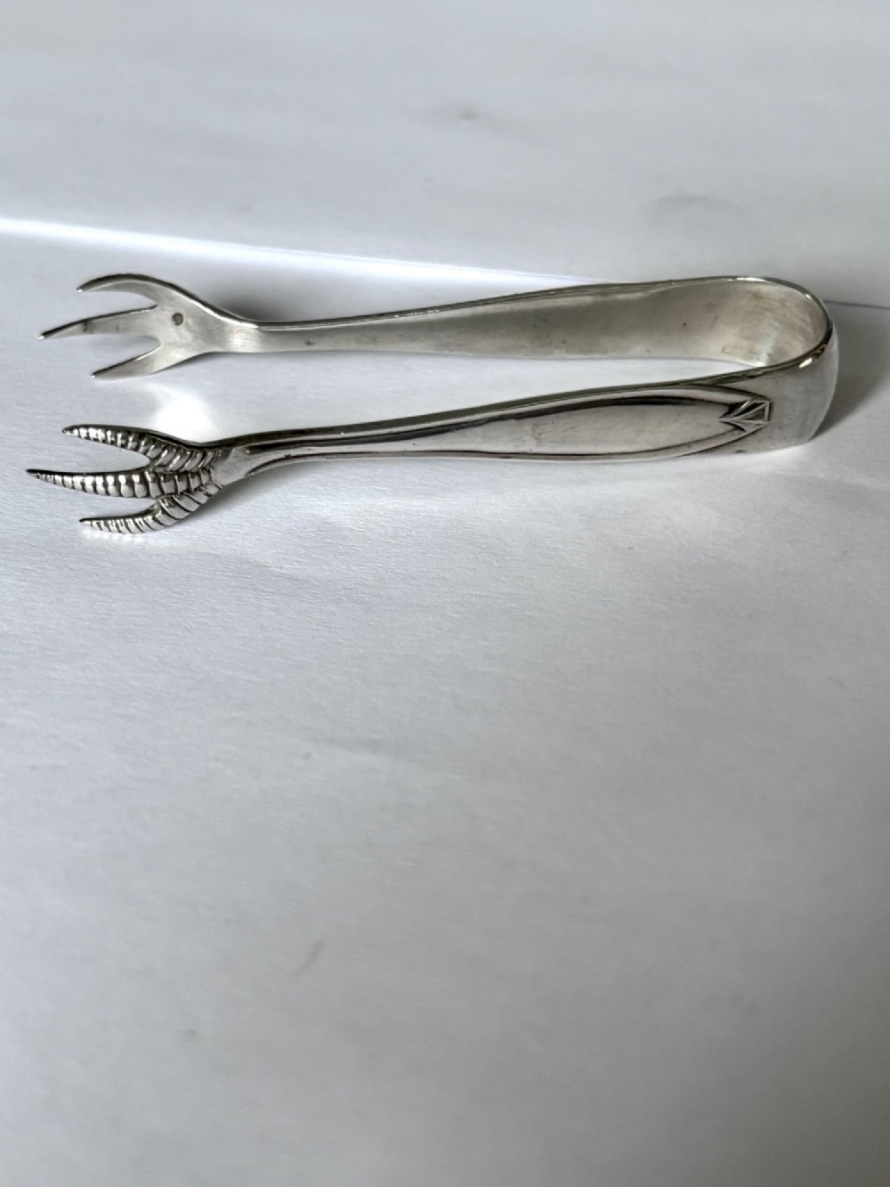 A pair of hallmarked sterling silver sugar nips featuring curved arms and claw-shaped grips resting on a light surface. View II