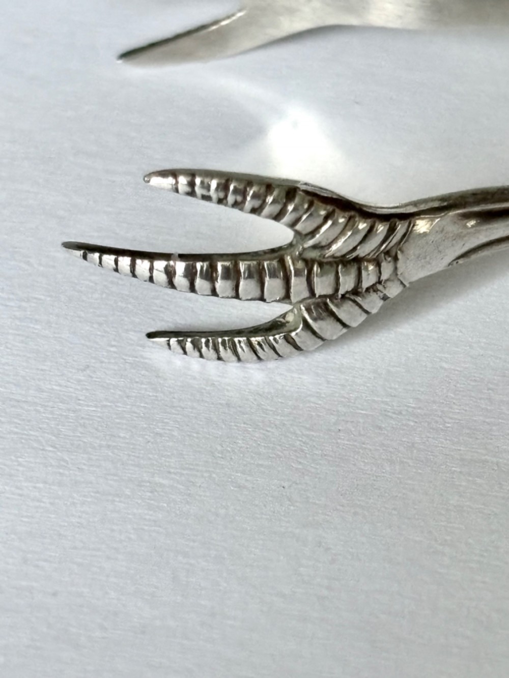 A pair of hallmarked sterling silver sugar nips featuring curved arms and claw-shaped grips resting on a light surface. View III