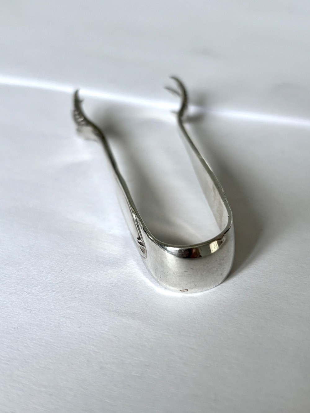 A pair of hallmarked sterling silver sugar nips featuring curved arms and claw-shaped grips resting on a light surface. View IV