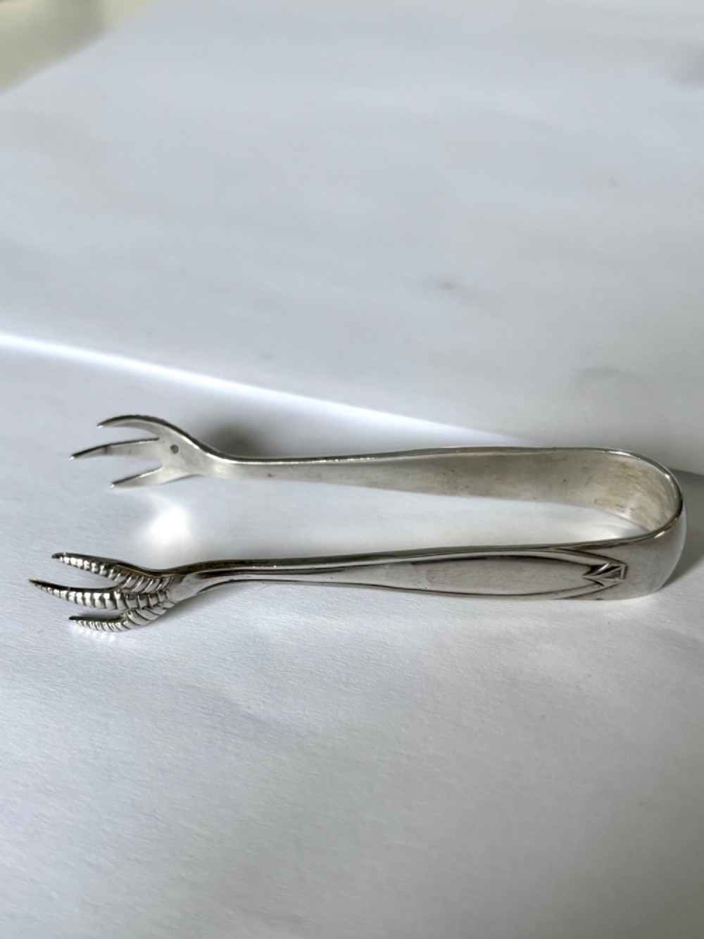 A pair of hallmarked sterling silver sugar nips featuring curved arms and claw-shaped grips resting on a light surface. View V