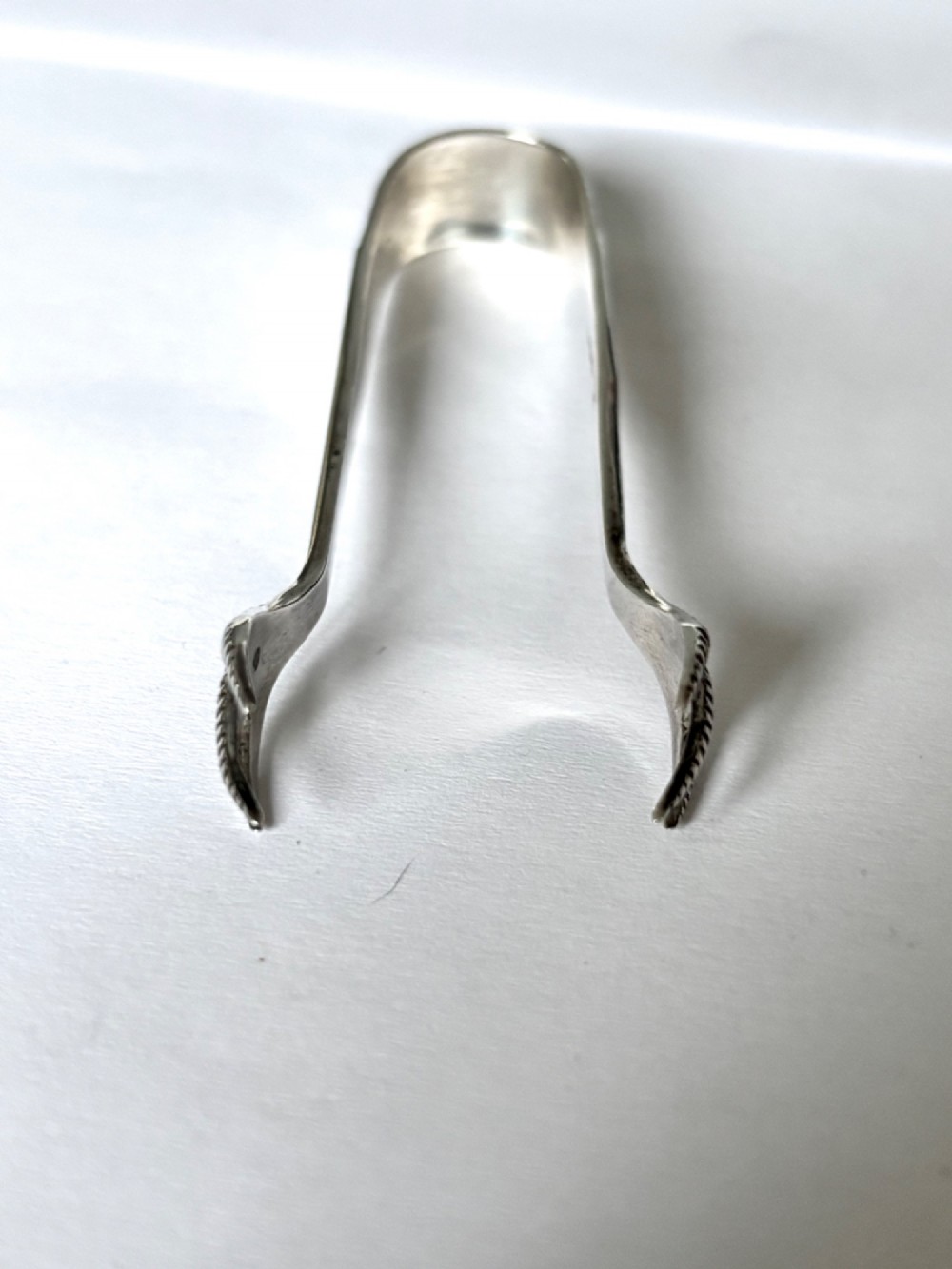 A pair of hallmarked sterling silver sugar nips featuring curved arms and claw-shaped grips resting on a light surface. View VI