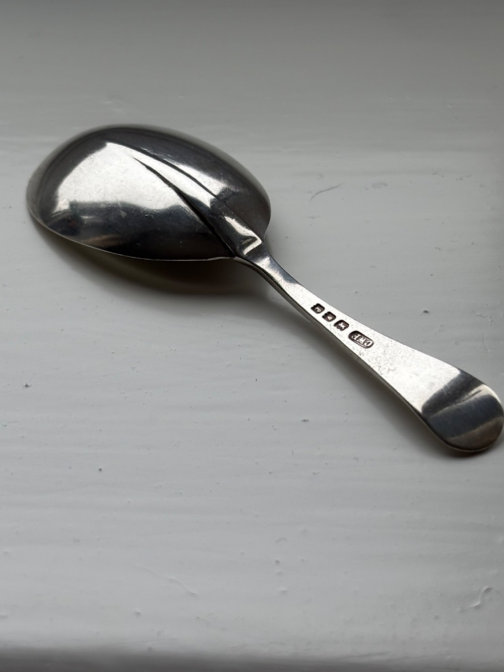 Underside view of a George V hallmarked sterling silver caddy spoon featuring a plain oval bowl and stamped hallmarks along the handle stem. View III