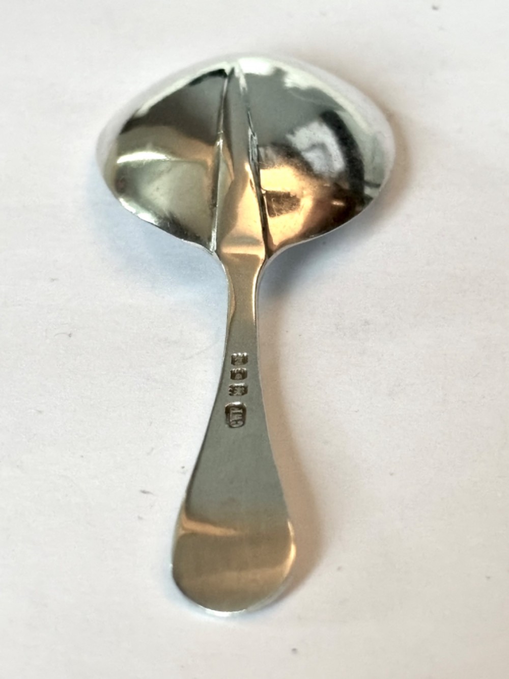 Underside view of a George V hallmarked sterling silver caddy spoon featuring a plain oval bowl and stamped hallmarks along the handle stem. View VI