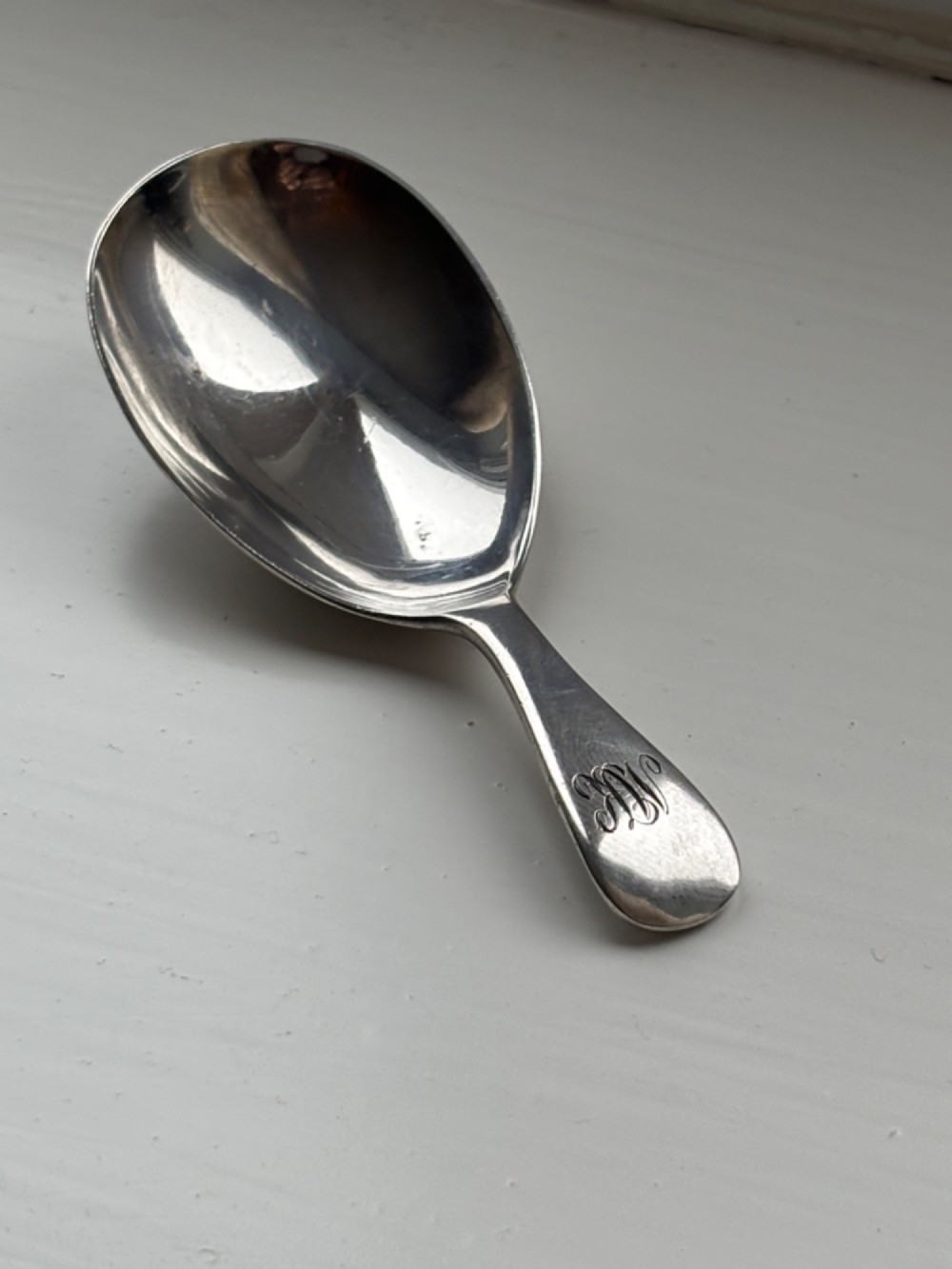 A George V sterling silver tea caddy spoon with a wide oval bowl and an engraved monogrammed handle.