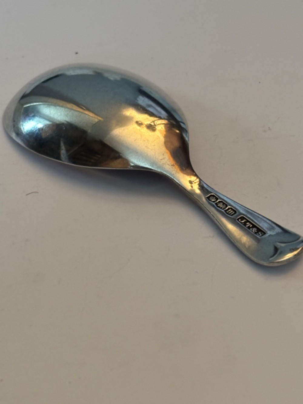 A George V sterling silver tea caddy spoon with a wide oval bowl and an engraved monogrammed handle. View IV