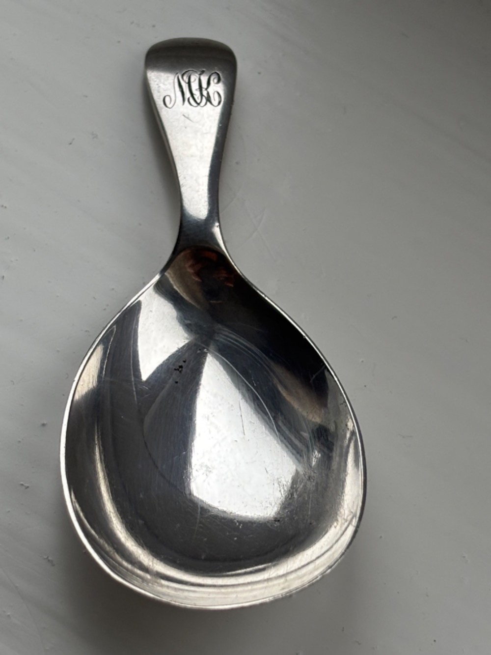 A George V sterling silver tea caddy spoon with a wide oval bowl and an engraved monogrammed handle. View V