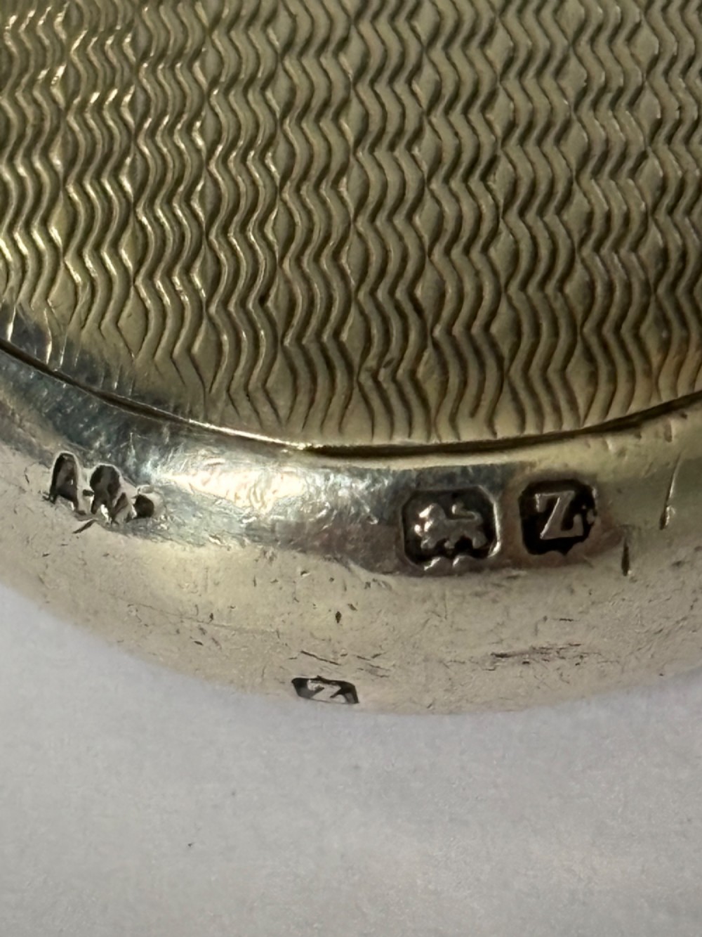 An oval sterling silver scent flask featuring an engine-turned pattern, a central engraved cartouche, a screw top cap, and British hallmarks at the base. View VIII