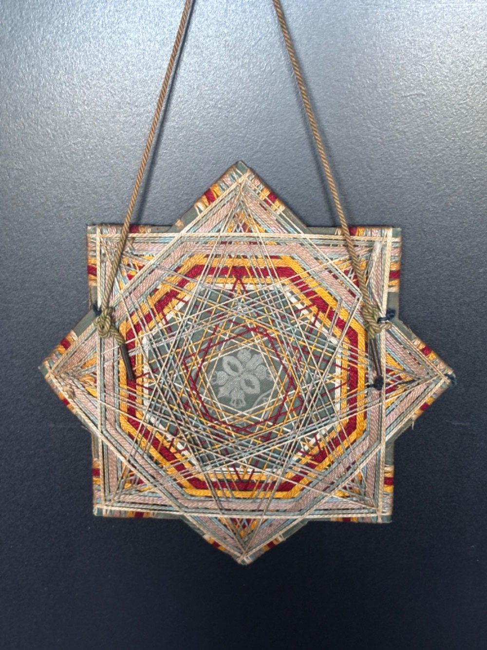 An octagram star-shaped folk art picture frame wrapped in beige, red, and gold string, surrounding a monochrome portrait photograph of five men. View II