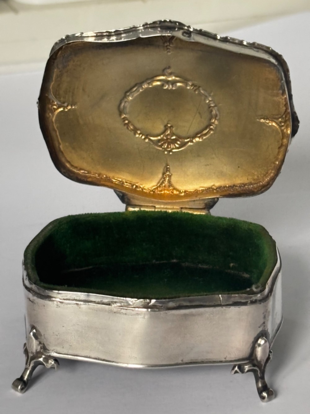 An open George V sterling silver trinket box featuring green velvet lining, gilt lid interior, and cabriole feet. View V