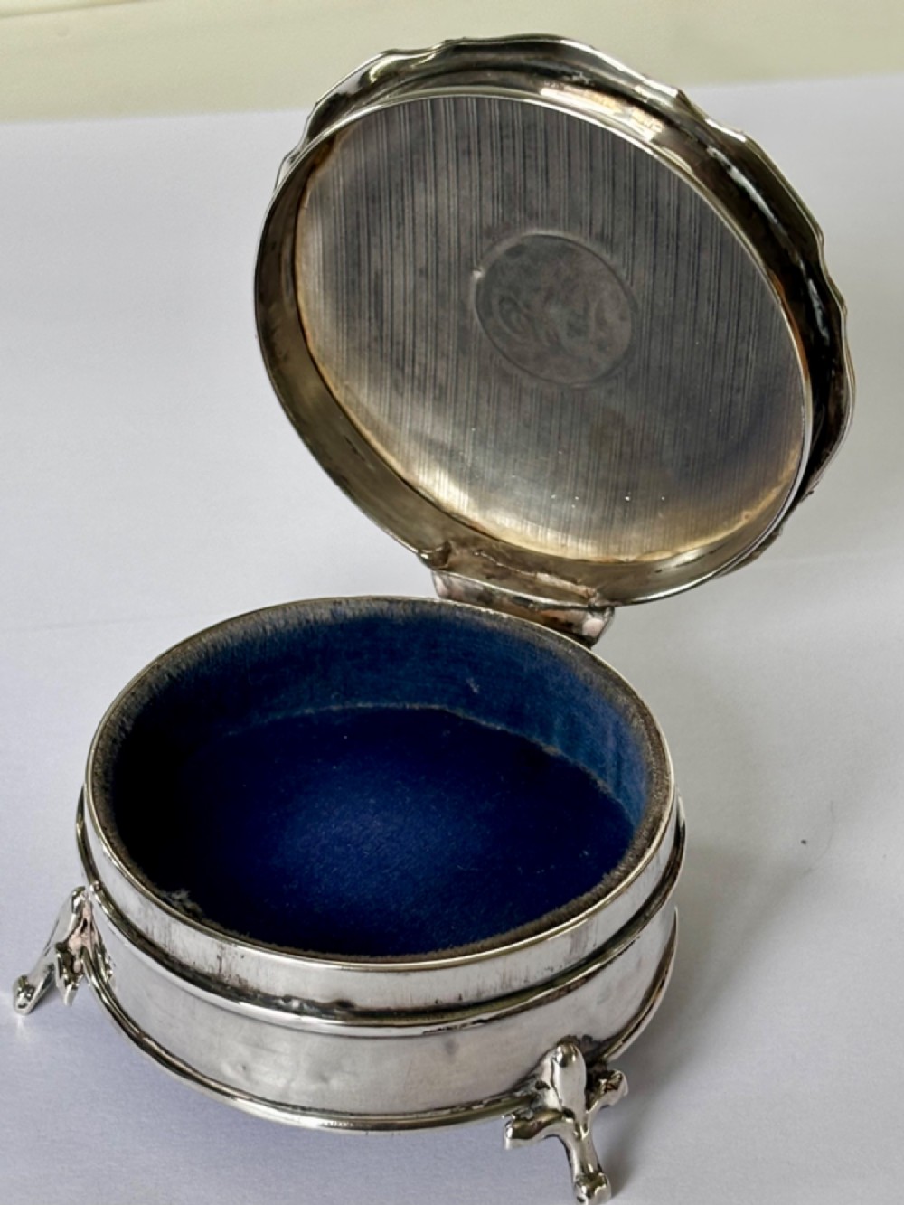 A circular George V sterling silver trinket box featuring engine-turned lid decoration, an engraved central cartouche, and four short pad feet. View III