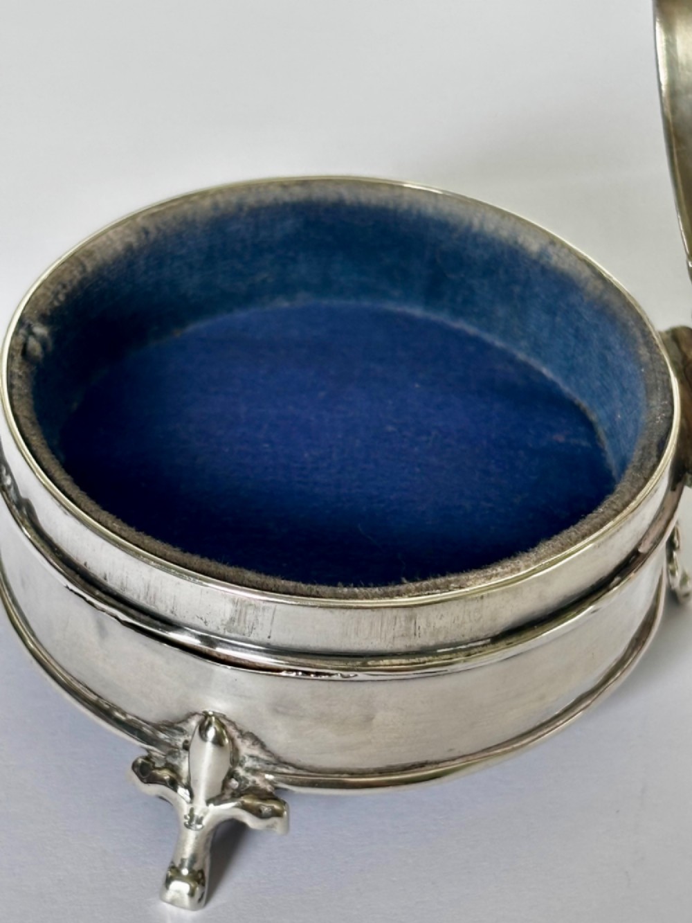 A circular George V sterling silver trinket box featuring engine-turned lid decoration, an engraved central cartouche, and four short pad feet. View IV