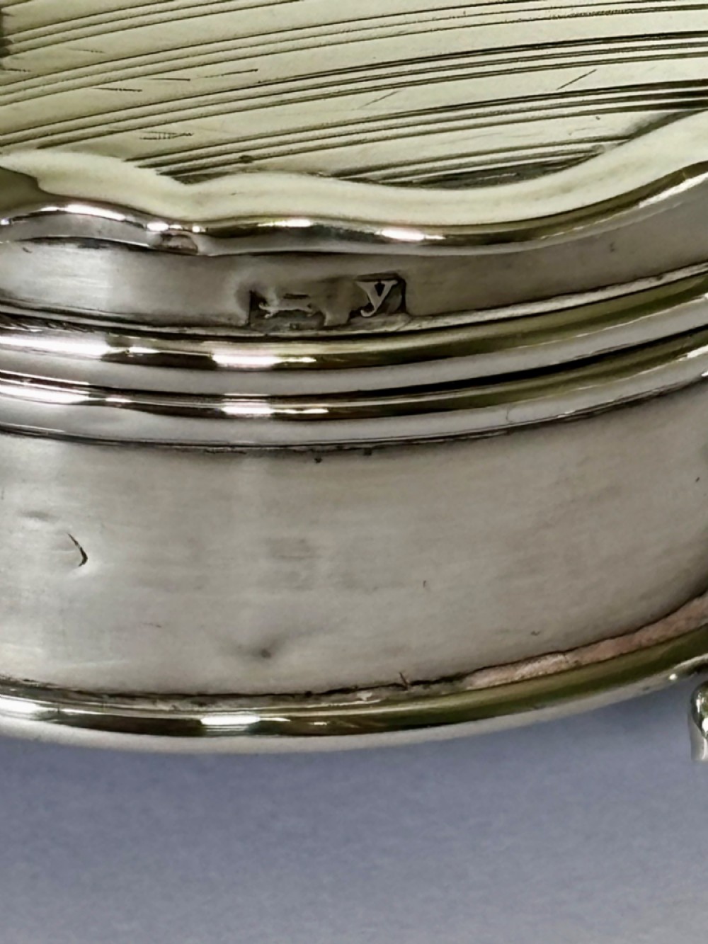 A circular George V sterling silver trinket box featuring engine-turned lid decoration, an engraved central cartouche, and four short pad feet. View VI