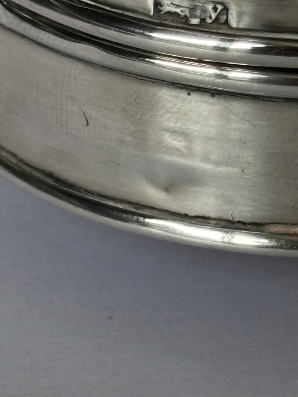 A circular George V sterling silver trinket box featuring engine-turned lid decoration, an engraved central cartouche, and four short pad feet. View IX