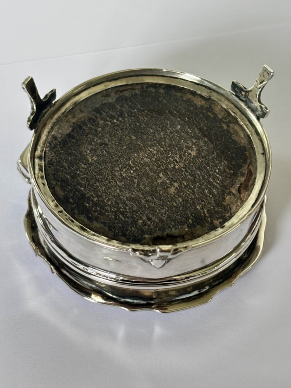 A circular George V sterling silver trinket box featuring engine-turned lid decoration, an engraved central cartouche, and four short pad feet. View X