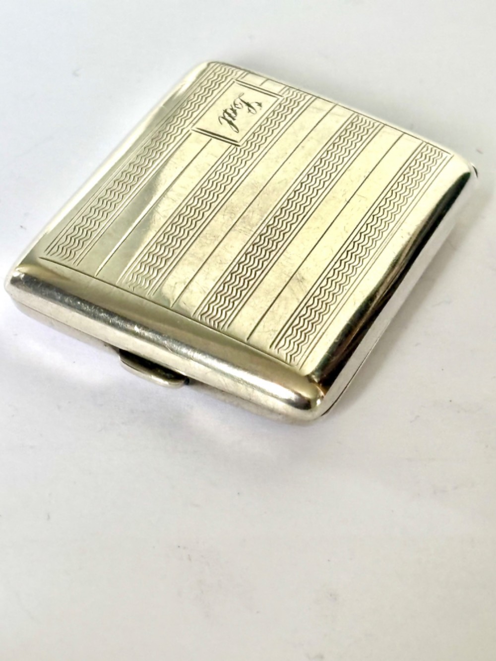 Rectangular sterling silver matchbook case featuring engine-turned geometric linear pattern and a central monogrammed cartouche. View II