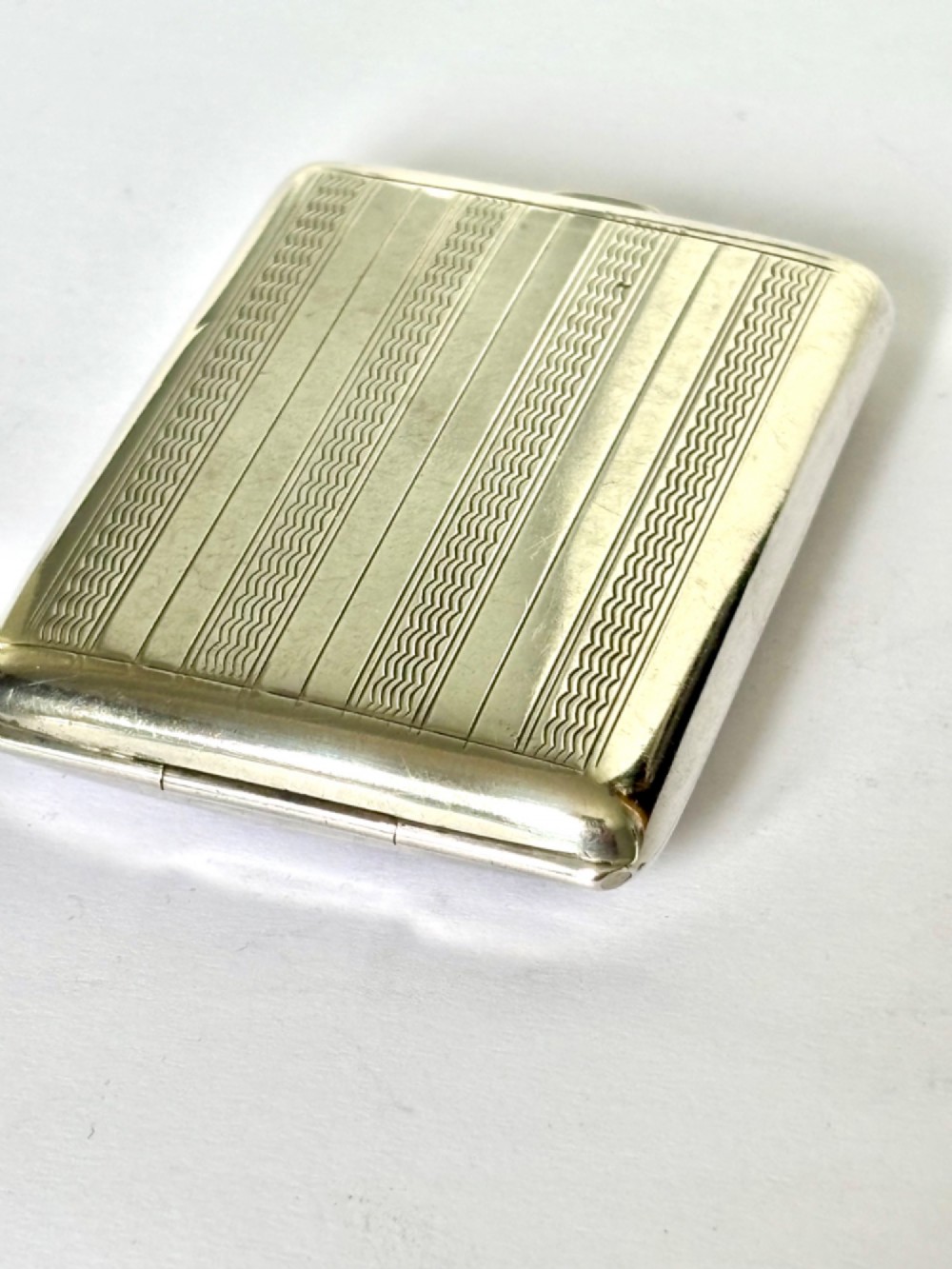 Rectangular sterling silver matchbook case featuring engine-turned geometric linear pattern and a central monogrammed cartouche. View III