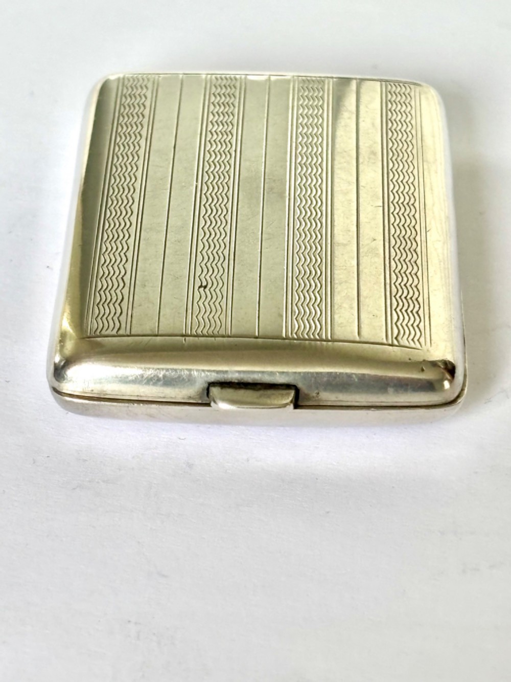 Rectangular sterling silver matchbook case featuring engine-turned geometric linear pattern and a central monogrammed cartouche. View IV