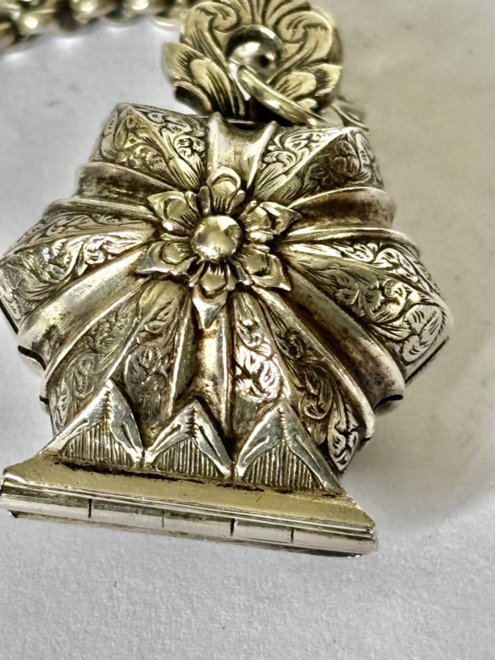 An antique silver white metal chatelaine featuring an ornate clip connected by links to five suspended grooming tools and a fluted vinaigrette container. View III