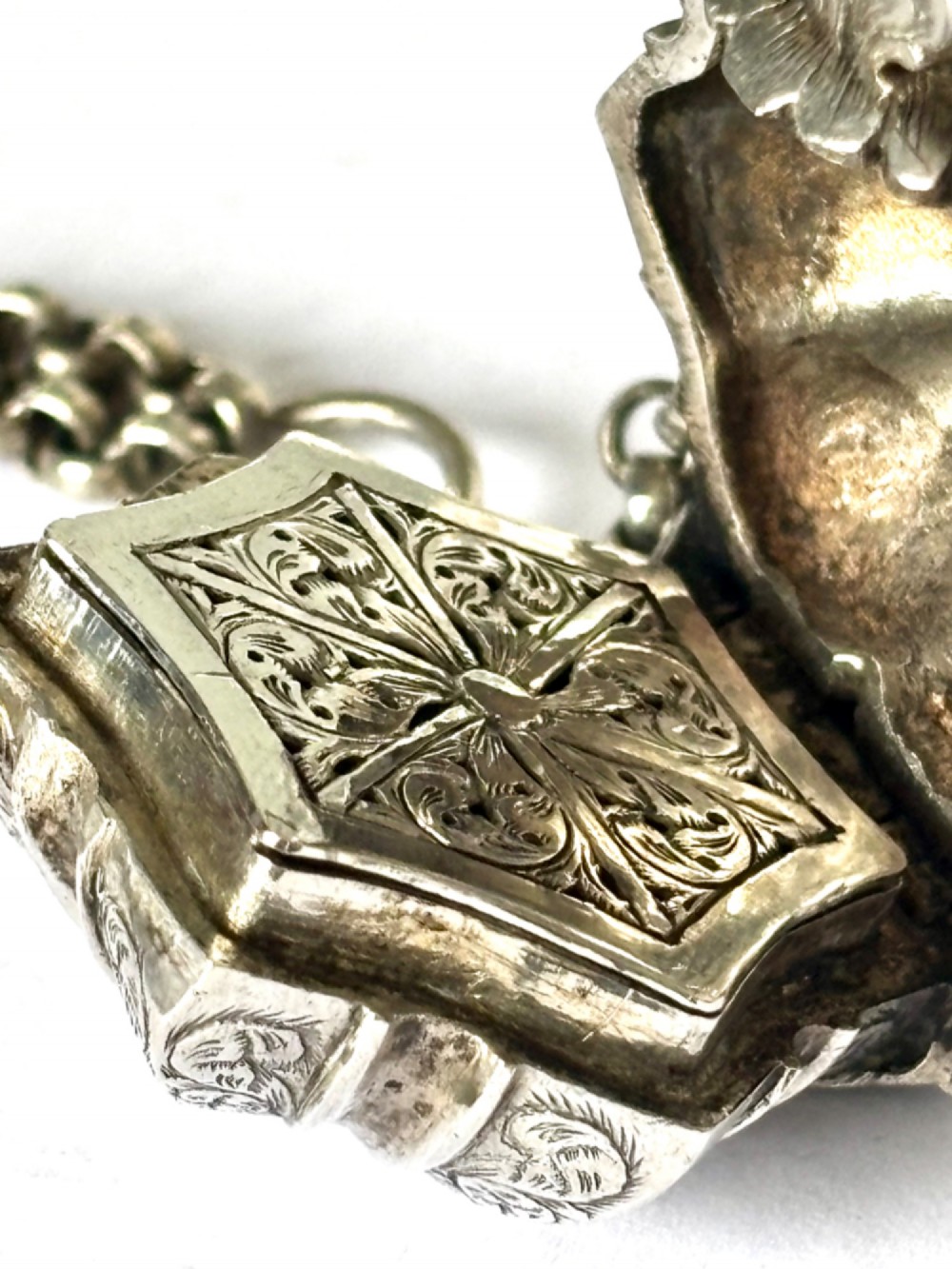 An antique silver white metal chatelaine featuring an ornate clip connected by links to five suspended grooming tools and a fluted vinaigrette container. View IV