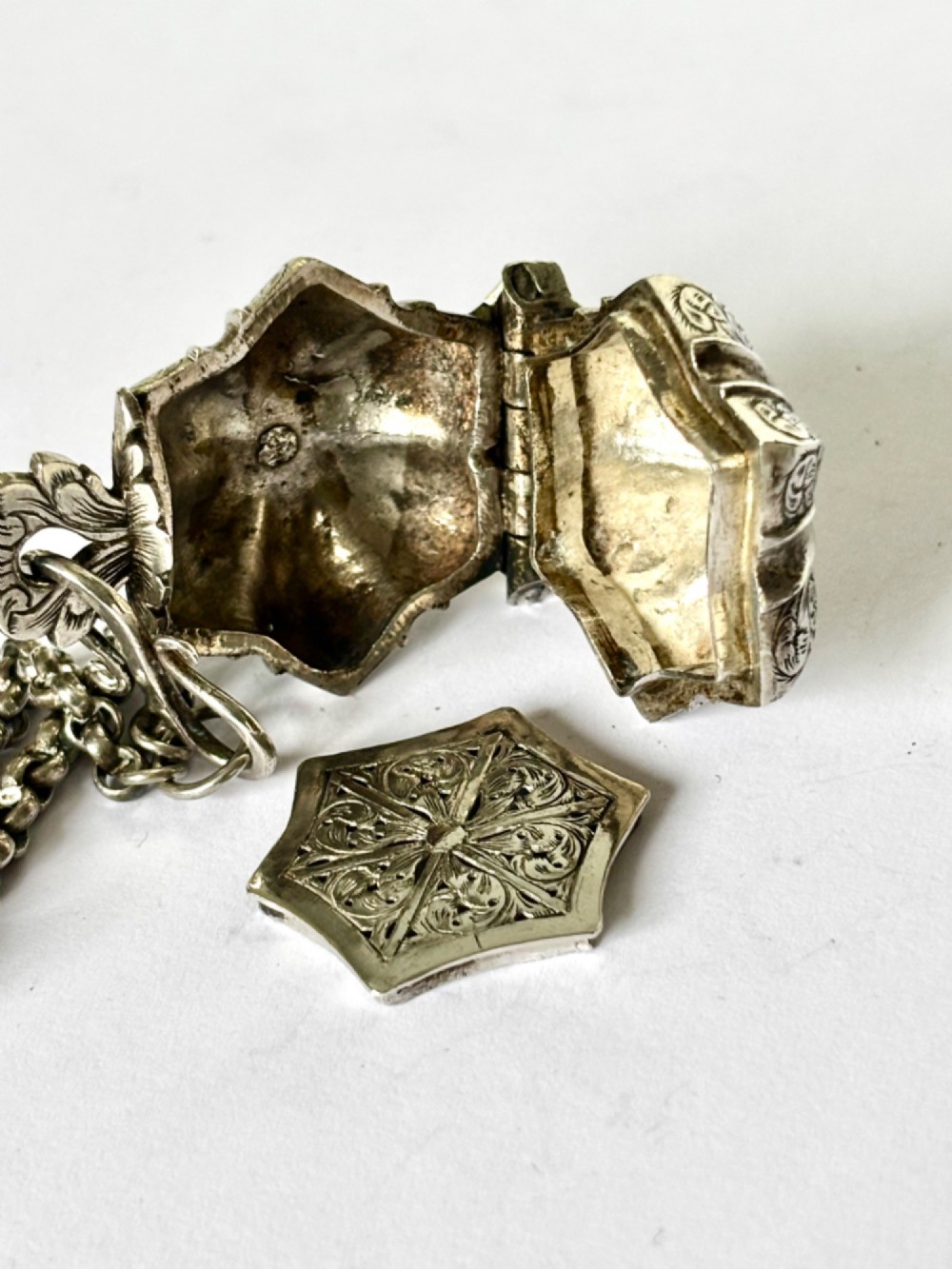 An antique silver white metal chatelaine featuring an ornate clip connected by links to five suspended grooming tools and a fluted vinaigrette container. View VI