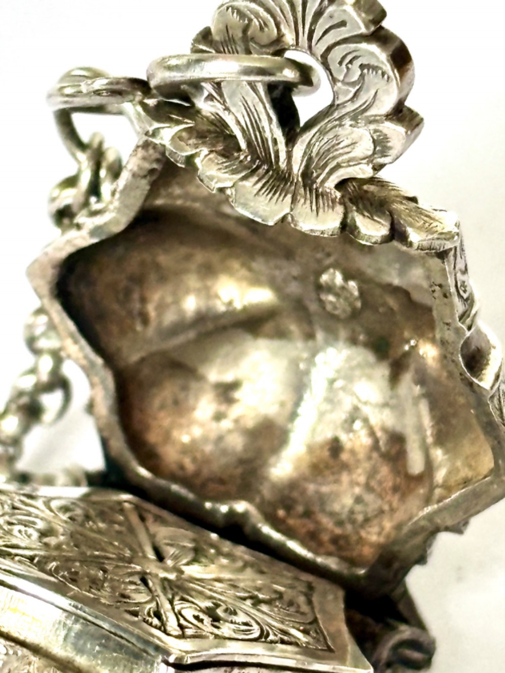 An antique silver white metal chatelaine featuring an ornate clip connected by links to five suspended grooming tools and a fluted vinaigrette container. View VII