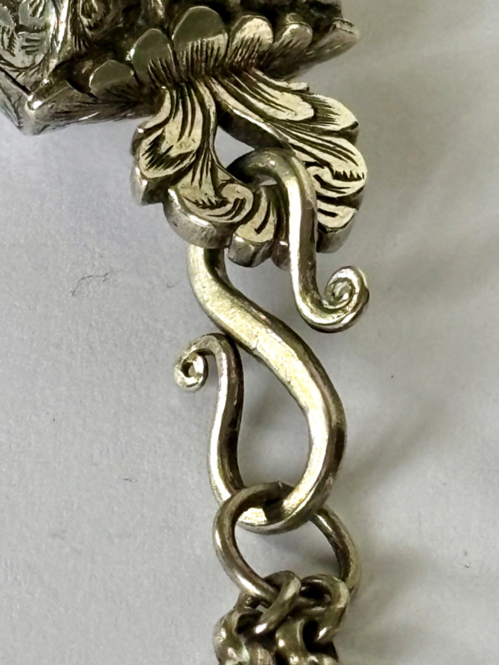 An antique silver white metal chatelaine featuring an ornate clip connected by links to five suspended grooming tools and a fluted vinaigrette container. View VIII