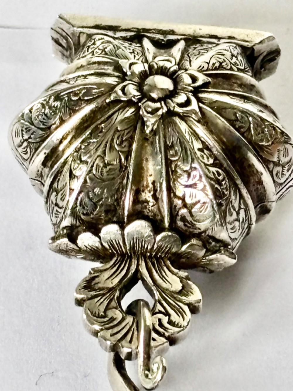 An antique silver white metal chatelaine featuring an ornate clip connected by links to five suspended grooming tools and a fluted vinaigrette container. View IX