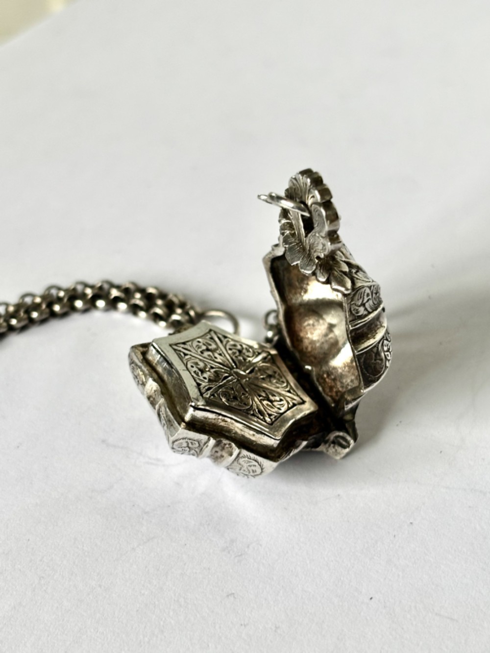 An antique silver white metal chatelaine featuring an ornate clip connected by links to five suspended grooming tools and a fluted vinaigrette container. View XII