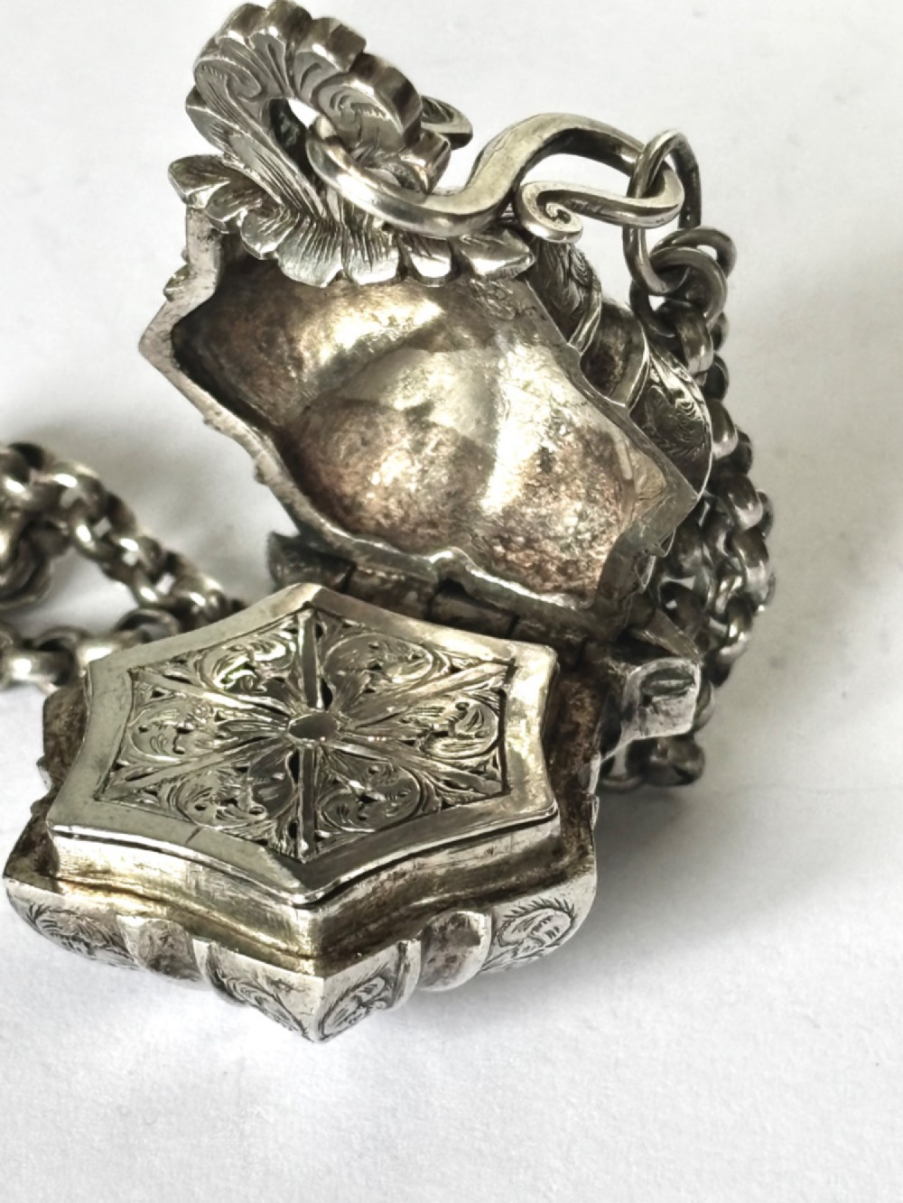 An antique silver white metal chatelaine featuring an ornate clip connected by links to five suspended grooming tools and a fluted vinaigrette container. View XIV