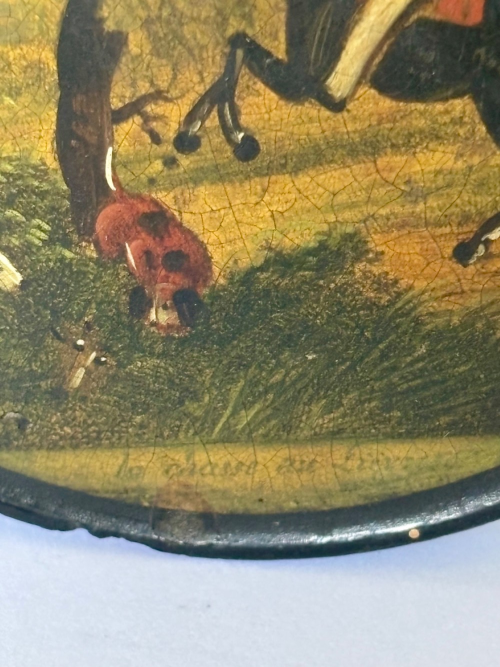 A circular black papier-mache snuff box featuring a hand-painted scene on the lid depicting a horseman and hunting dogs. View III