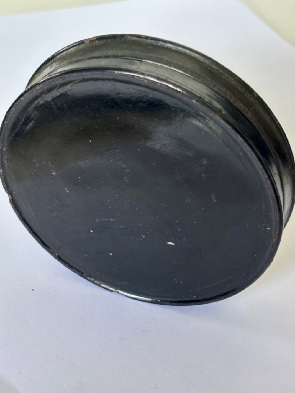 A circular black papier-mache snuff box featuring a hand-painted scene on the lid depicting a horseman and hunting dogs. View VI