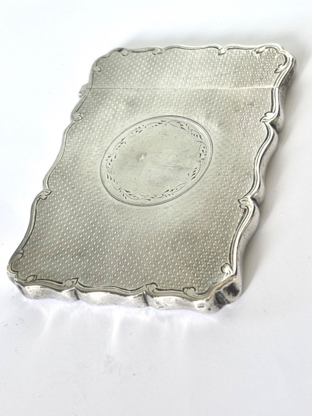 An antique Victorian sterling silver calling card case featuring shaped wavy edges, an engine-turned pattern, and an oval central cartouche. View II