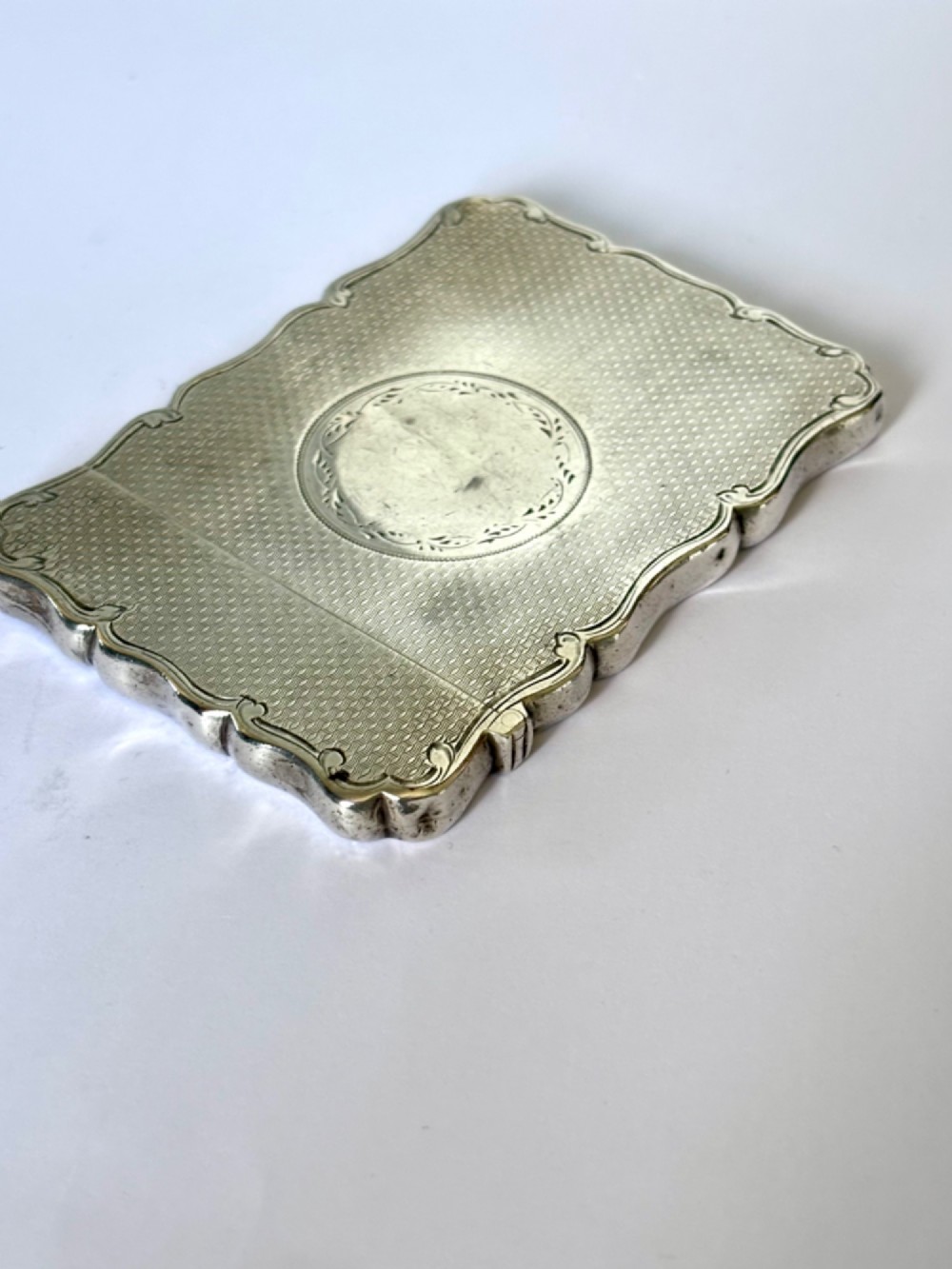 An antique Victorian sterling silver calling card case featuring shaped wavy edges, an engine-turned pattern, and an oval central cartouche. View IV