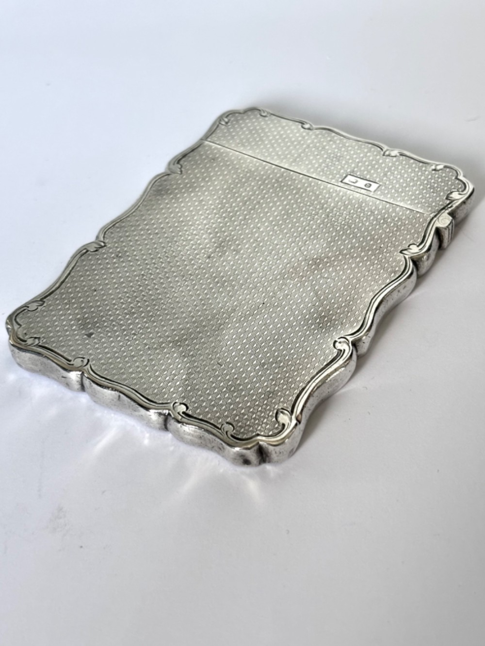 An antique Victorian sterling silver calling card case featuring shaped wavy edges, an engine-turned pattern, and an oval central cartouche. View V