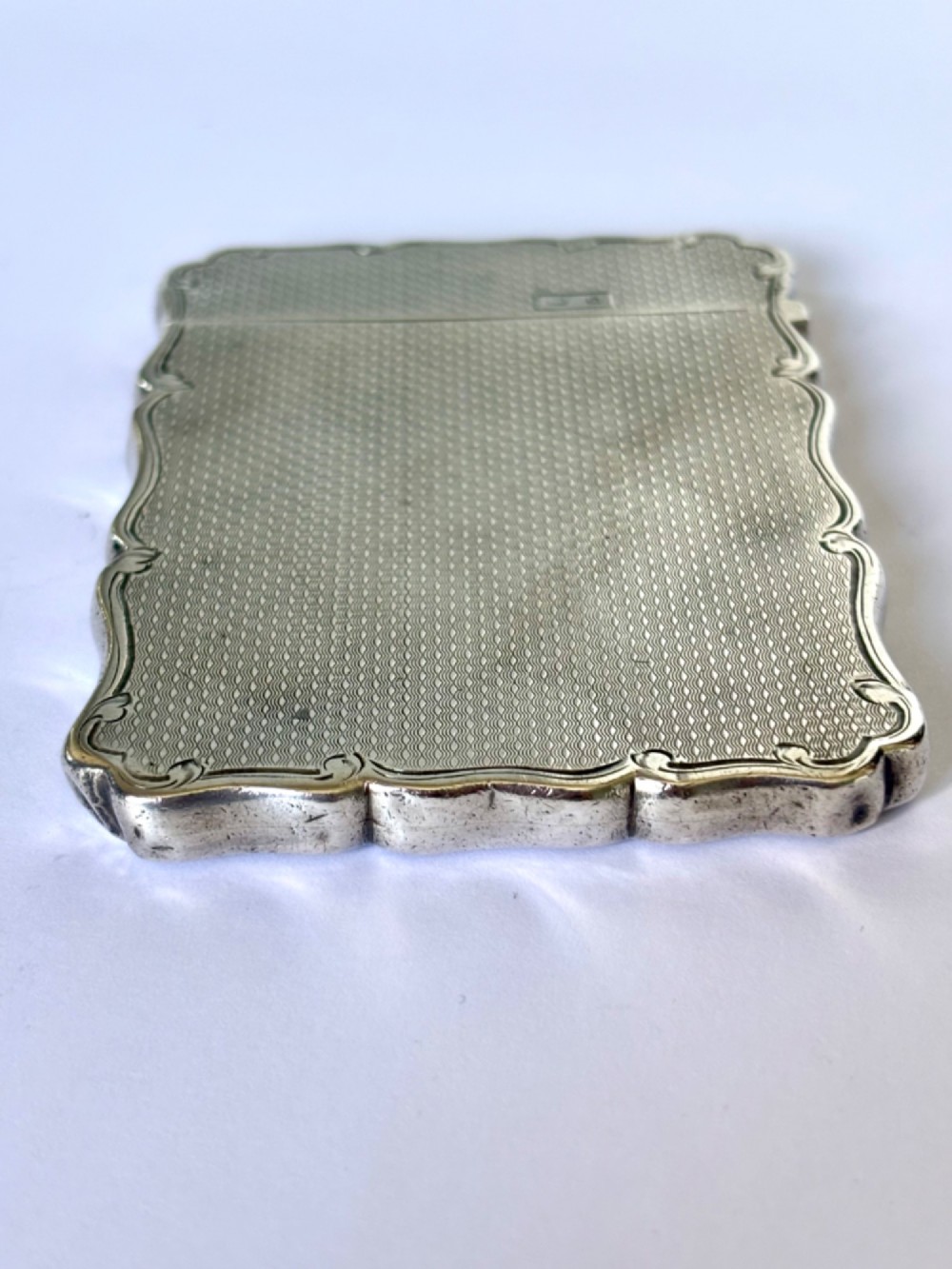An antique Victorian sterling silver calling card case featuring shaped wavy edges, an engine-turned pattern, and an oval central cartouche. View VI