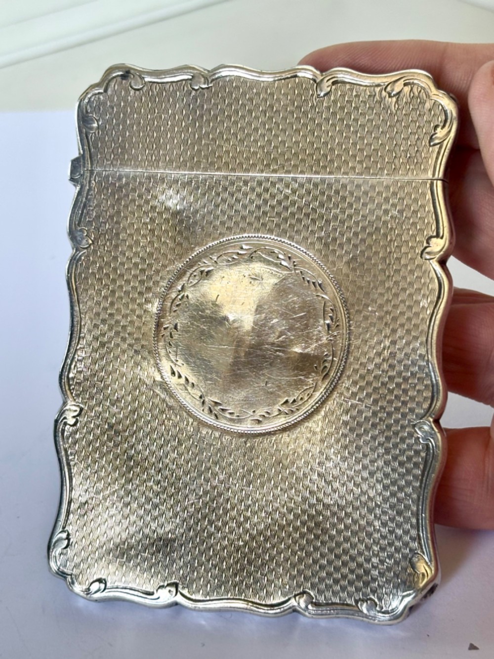 An antique Victorian sterling silver calling card case featuring shaped wavy edges, an engine-turned pattern, and an oval central cartouche. View X