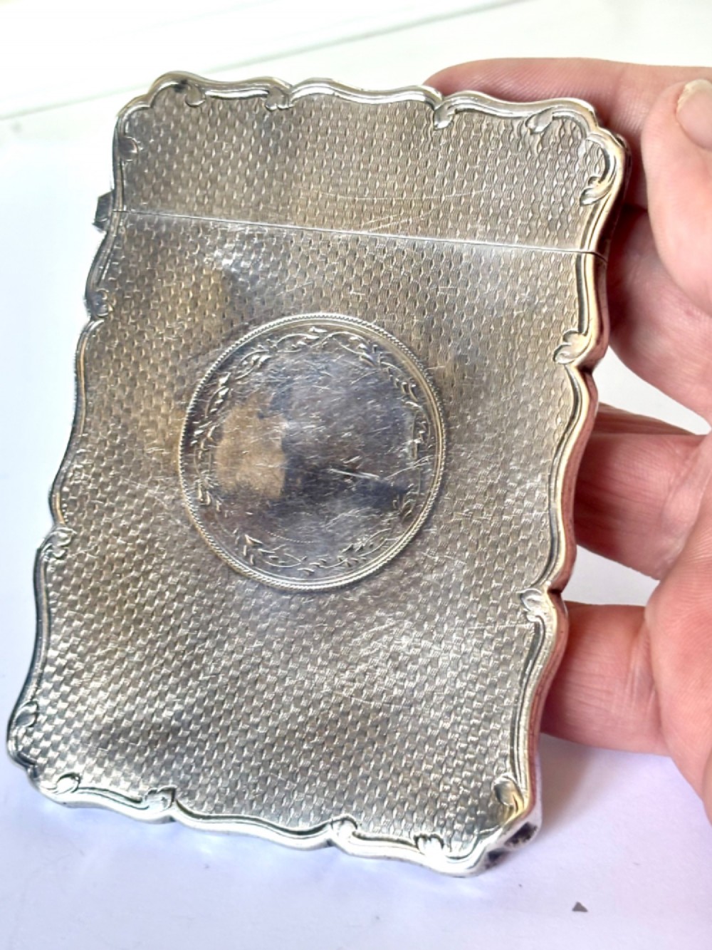 An antique Victorian sterling silver calling card case featuring shaped wavy edges, an engine-turned pattern, and an oval central cartouche. View XII