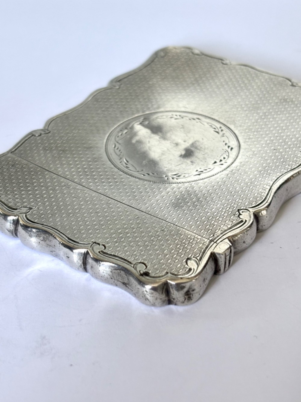 An antique Victorian sterling silver calling card case featuring shaped wavy edges, an engine-turned pattern, and an oval central cartouche. View XIV