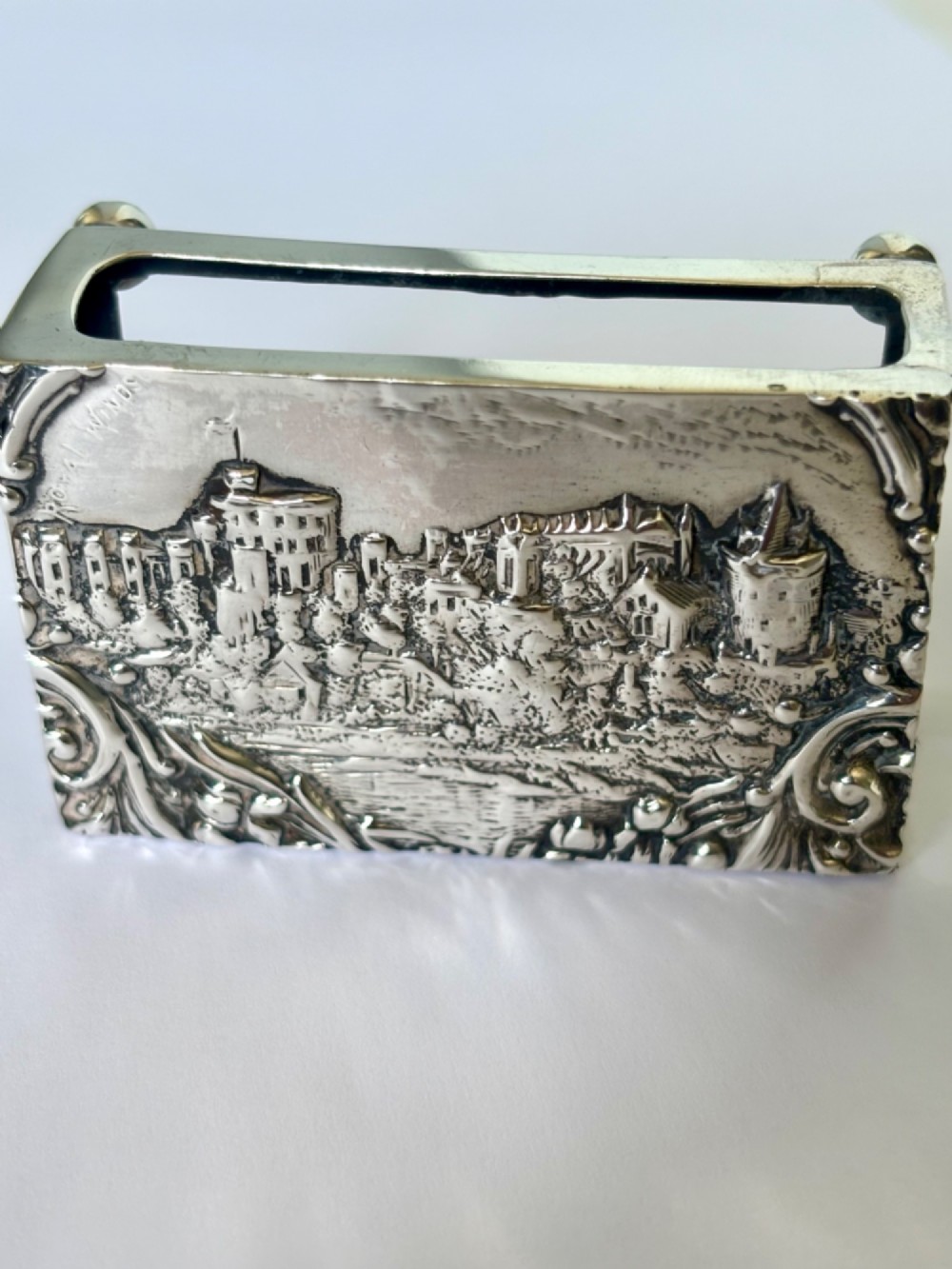 A rectangular silver matchbox cover featuring an embossed relief depicting Windsor Castle surrounded by scrollwork borders.