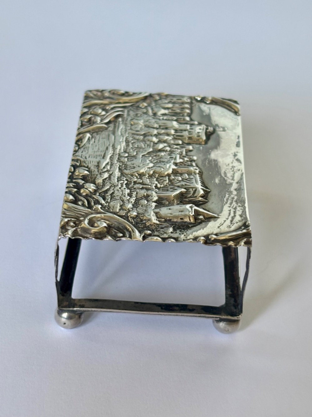 A rectangular silver matchbox cover featuring an embossed relief depicting Windsor Castle surrounded by scrollwork borders. View V