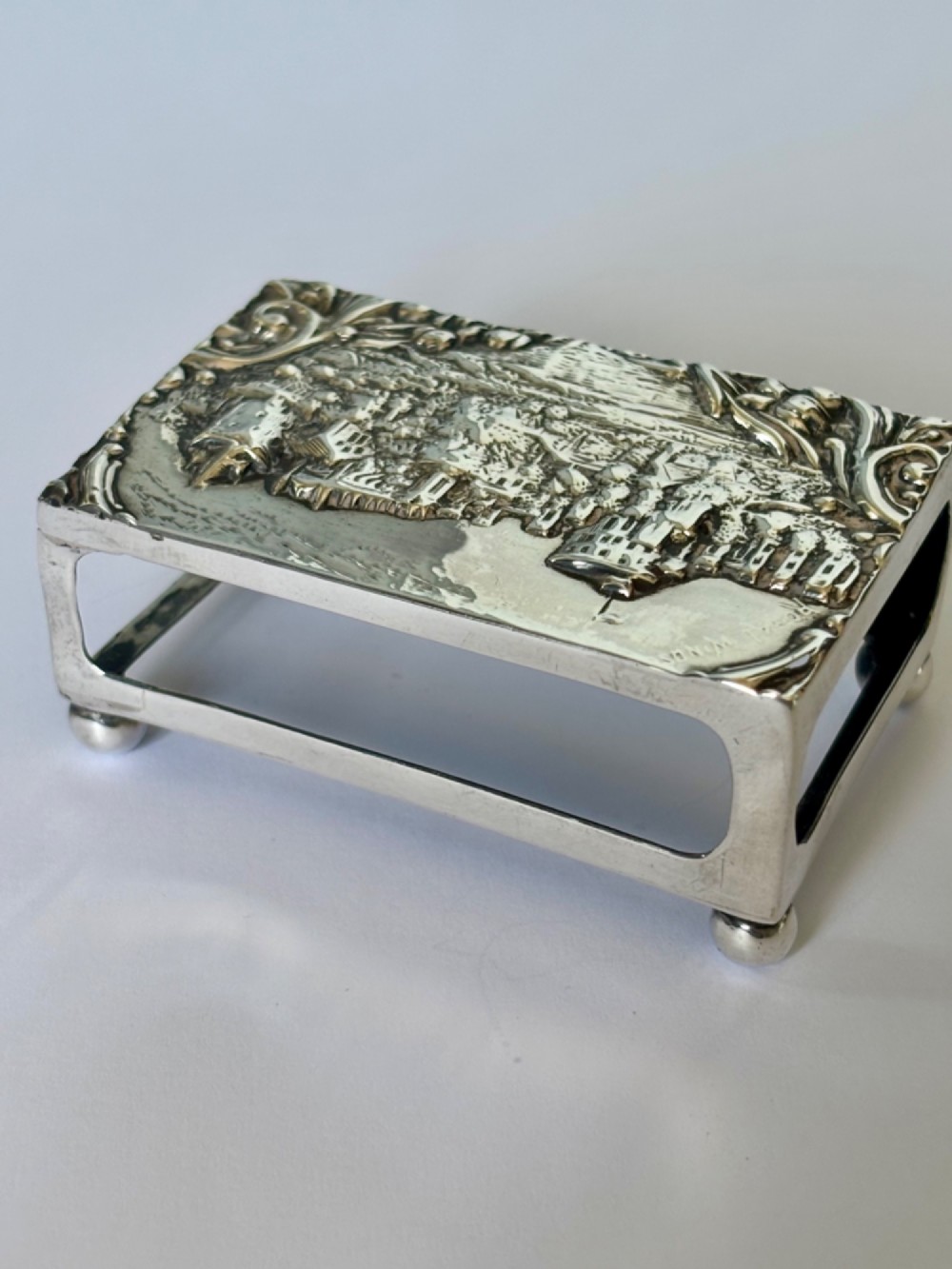 A rectangular silver matchbox cover featuring an embossed relief depicting Windsor Castle surrounded by scrollwork borders. View VI