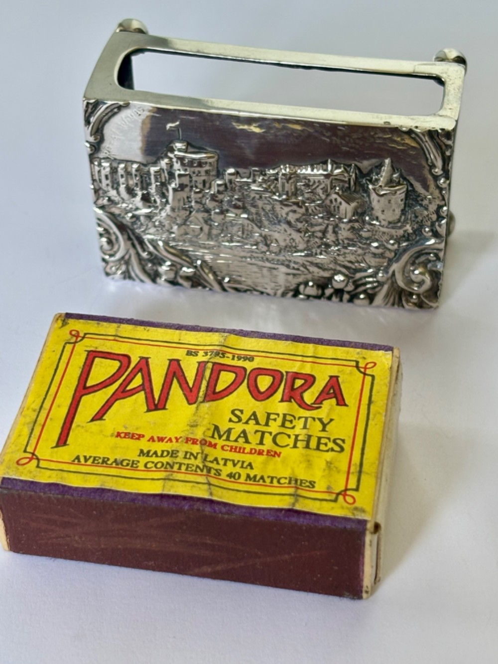 A rectangular silver matchbox cover featuring an embossed relief depicting Windsor Castle surrounded by scrollwork borders. View IX