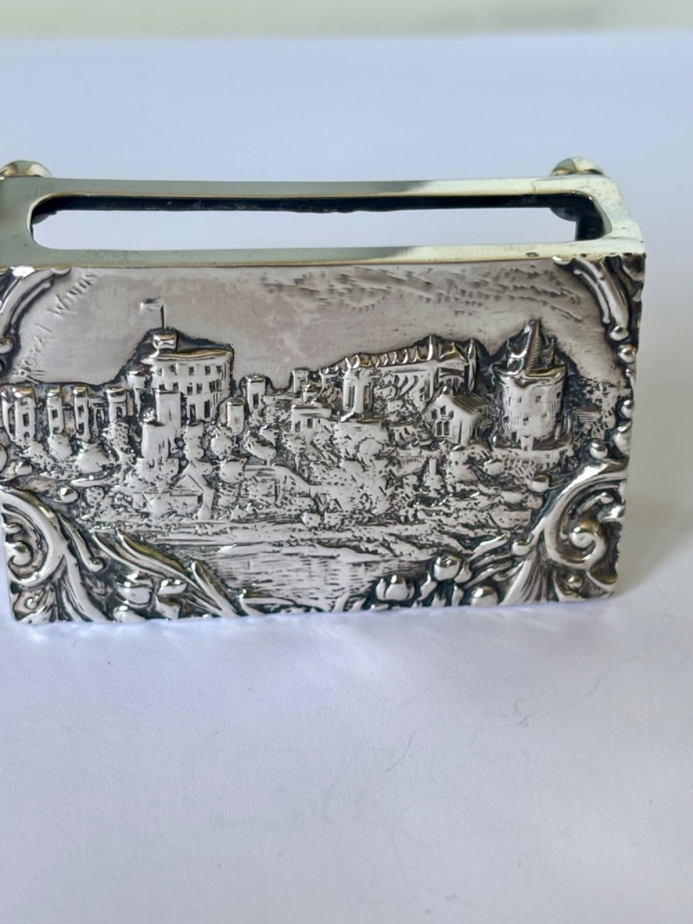 A rectangular silver matchbox cover featuring an embossed relief depicting Windsor Castle surrounded by scrollwork borders. View X
