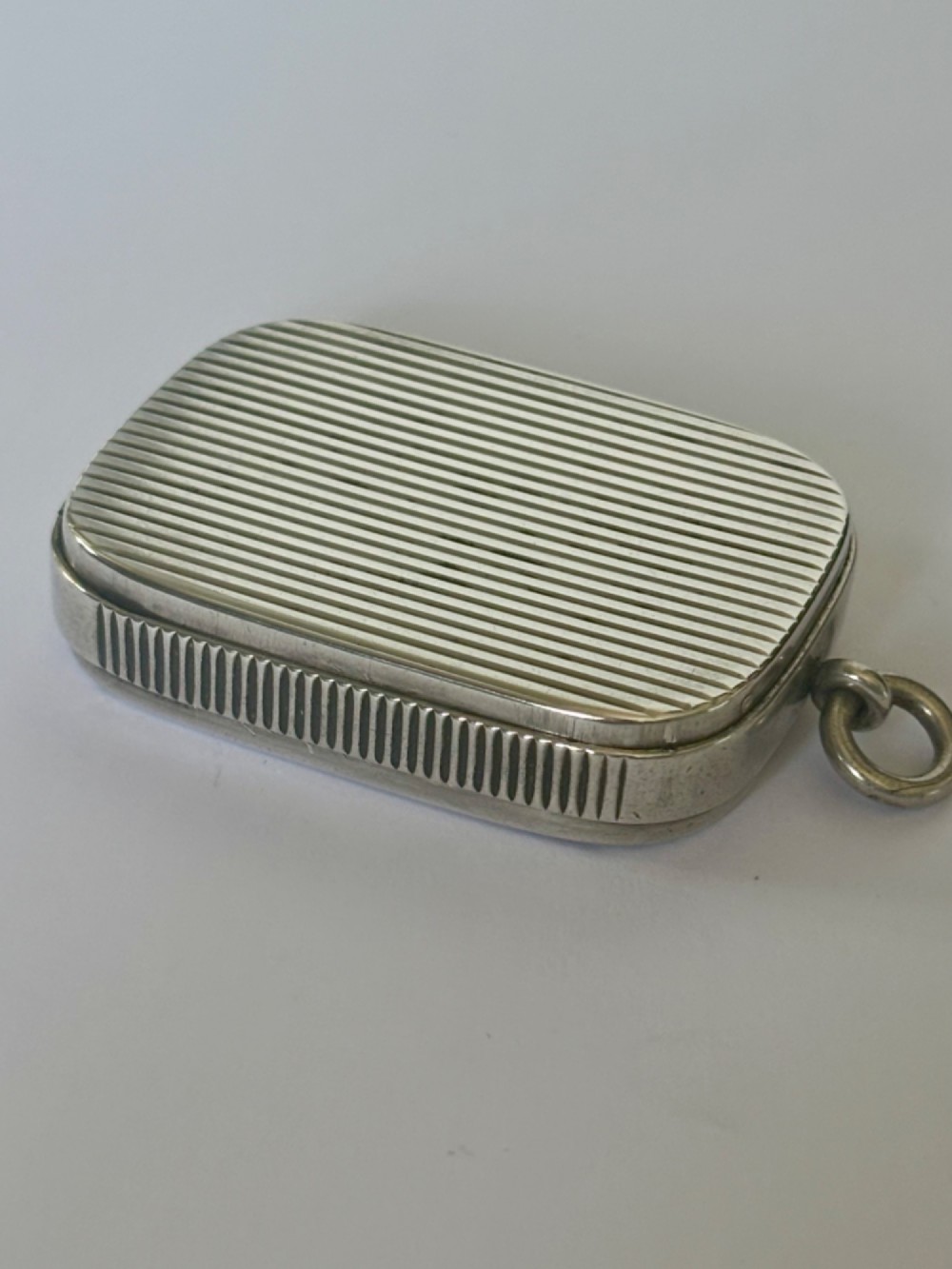 A small rectangular Victorian silver vesta case featuring horizontal reeded engine-turned decoration and an attached side suspension ring.